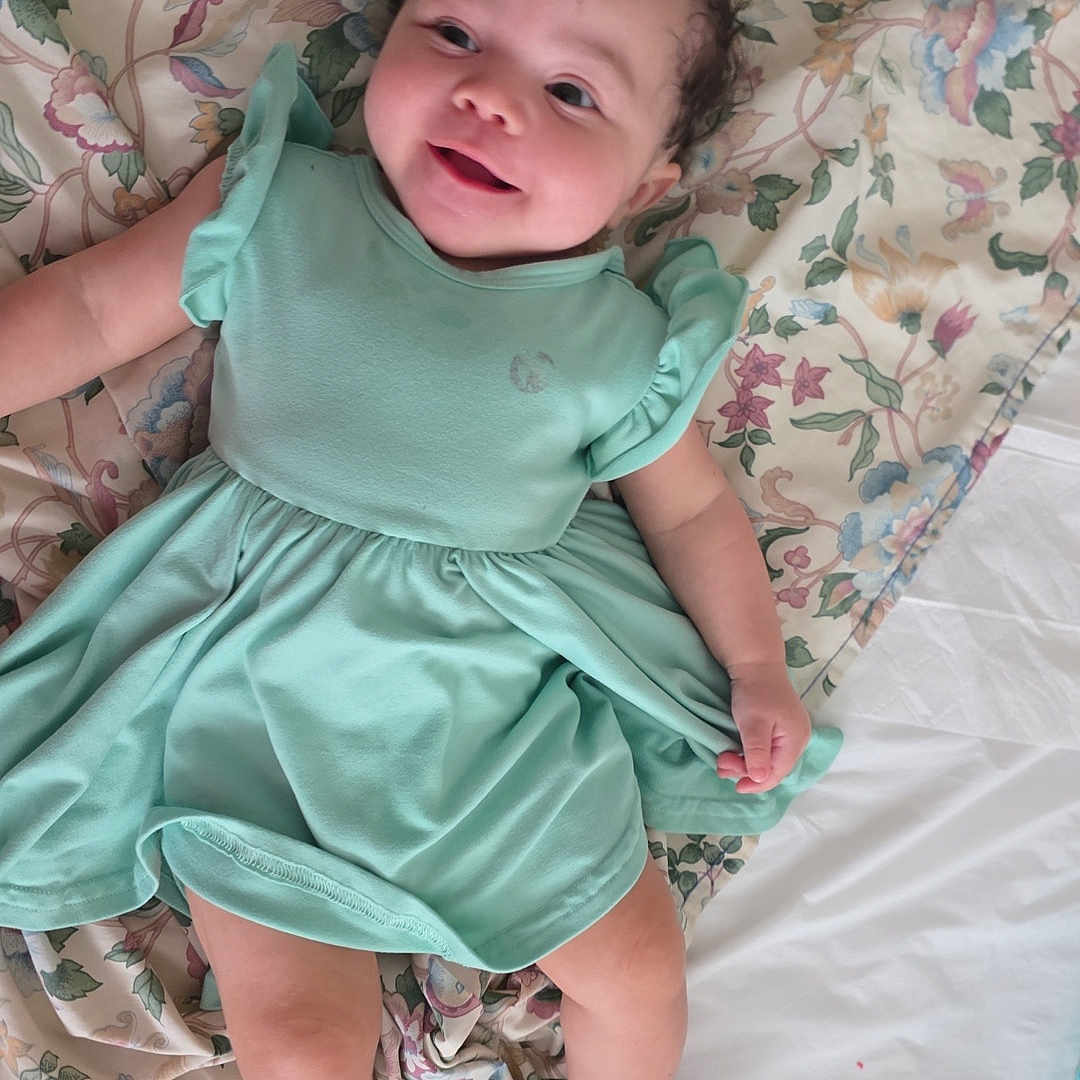 Natalia joined the competition — help win amazing prizes! baby, smiling, mint_green_dress, blanket, floral_pattern, lying_down, bed, happy, infant, cute, child, skin, foot, hand, curly_hair, indoors, portrait, toddler, clothing, resting