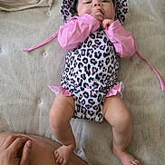 Natalia is registered to the contest to win money with this photo: baby, infant, child, pink_clothing, leopard_print, hat, sucking_fingers, lying_down, hand, leg, skin, cute, relaxed, indoors, fabric, pattern, person, baby_outfit, newborn, soft_light