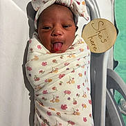 Zurilei joined the competition — help win amazing prizes! newborn, baby, infant, swaddle, headband, tongue_out, hospital_bassinet, wooden_sign, floral_pattern, cute, sleepwear, person, child, infant_care, hospital, bed, blanket, skin, face, expression
