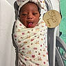 baby, bed, blanket, child, cute, expression, face, floral_pattern, headband, hospital, hospital_bassinet, infant, infant_care, newborn, person, skin, sleepwear, swaddle, tongue_out, wooden_sign
