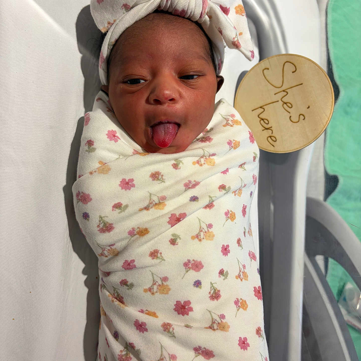 Zurilei joined the competition — help win amazing prizes! newborn, baby, infant, swaddle, headband, tongue_out, hospital_bassinet, wooden_sign, floral_pattern, cute, sleepwear, person, child, infant_care, hospital, bed, blanket, skin, face, expression