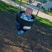 Harley is registered to the contest to win money with this photo: baby, swing, playground, child, outdoor, park, grass, trees, residential, daytime, blue_clothing, infant, seat, chain, woodchips, curious, person, sunlight, casual, expression