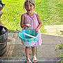 Tinley is registered to the contest to win money with this photo: barrel, basket, casual, child, daylight, expression, footwear, girl, grass, happy, holding, nature, outdoor, pink_dress, plant, sandals, sidewalk, summer, wooden_porch, young