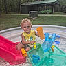 Cain joined the competition — help win amazing prizes! toddler, child, pool, water_toys, slide, outdoor, grass, trees, greenery, play, summer, yellow_shirt, curly_hair, toy_cup, plastic, recreation, nature, daylight, happy, fun