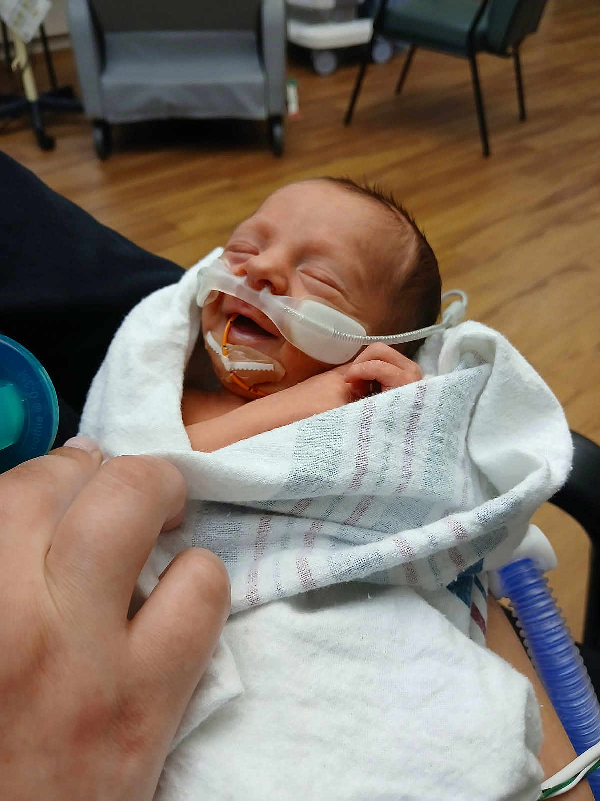 Raymond is registered to the contest to win money with this photo: newborn, baby, infant, blanket, hospital, medical_tube, sleeping, hand, person, healthcare, care, wrapped, face, peaceful, wood_floor, chair, medical_equipment, closeup, indoors, patient