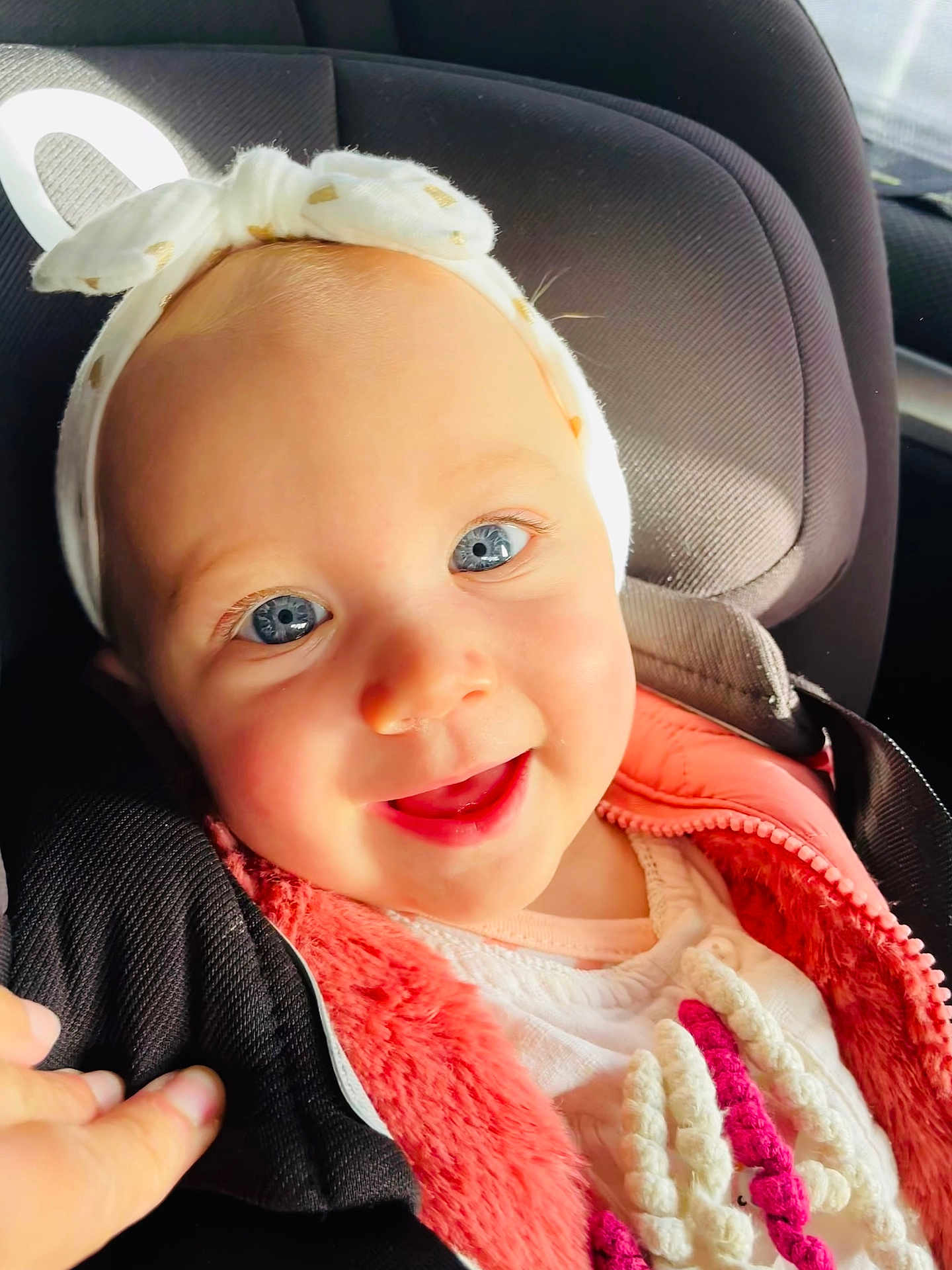 Mïa participe au concours pour gagner de l'argent avec cette photo : baby, child, blue_eyes, headband, car_seat, pink_jacket, white_clothing, smiling, happy, closeup, portrait, infant, cute, hand, warm_clothing, seatbelt, indoors, sunlight, human, face