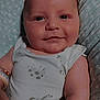 baby, infant, smiling, face, arm, onesie, clothing, cushion, pattern, soft_texture, close_up, comfort, child, cute, indoor, portrait, skin, expression, happy, newborn