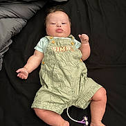 Karsten is registered to the contest to win money with this photo: arms, baby, bed, black_background, blanket, child, clothing, cute, expression, face, indoor, infant, legs, lying_down, overalls, pacifier, person, skin, soft_lighting, young_child