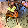 braided_hair, child, cute, daylight, floor, furniture, happy, home, indoor, kitchen, person, plastic_bag, sitting, smiling, table, tiled_floor, toddler, water_bottle, wooden_chair, yellow_outfit