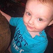 Madalynn is registered to the contest to win money with this photo: baby, blue_shirt, casual_clothing, child, couch, cute, expression, eyes, face, furniture, happy, head, indoor, infant, person, portrait, skin, smiling, text_on_clothing, young_child