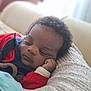 baby, sleeping, infant, curly_hair, red_clothing, knitted_pillow, hand_on_face, close_up, cozy, resting, indoors, portrait, peaceful, child, young, soft_light, relaxing, cute, warm, comfort