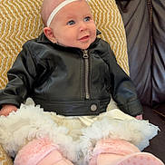 Araya is registered to the contest to win money with this photo: baby, infant, leather_jacket, pink_booties, headband, couch, pillow, smile, blue_eyes, sitting, indoor, clothing, cute, portrait, child, soft_toys, fashion, leather, happy, cozy