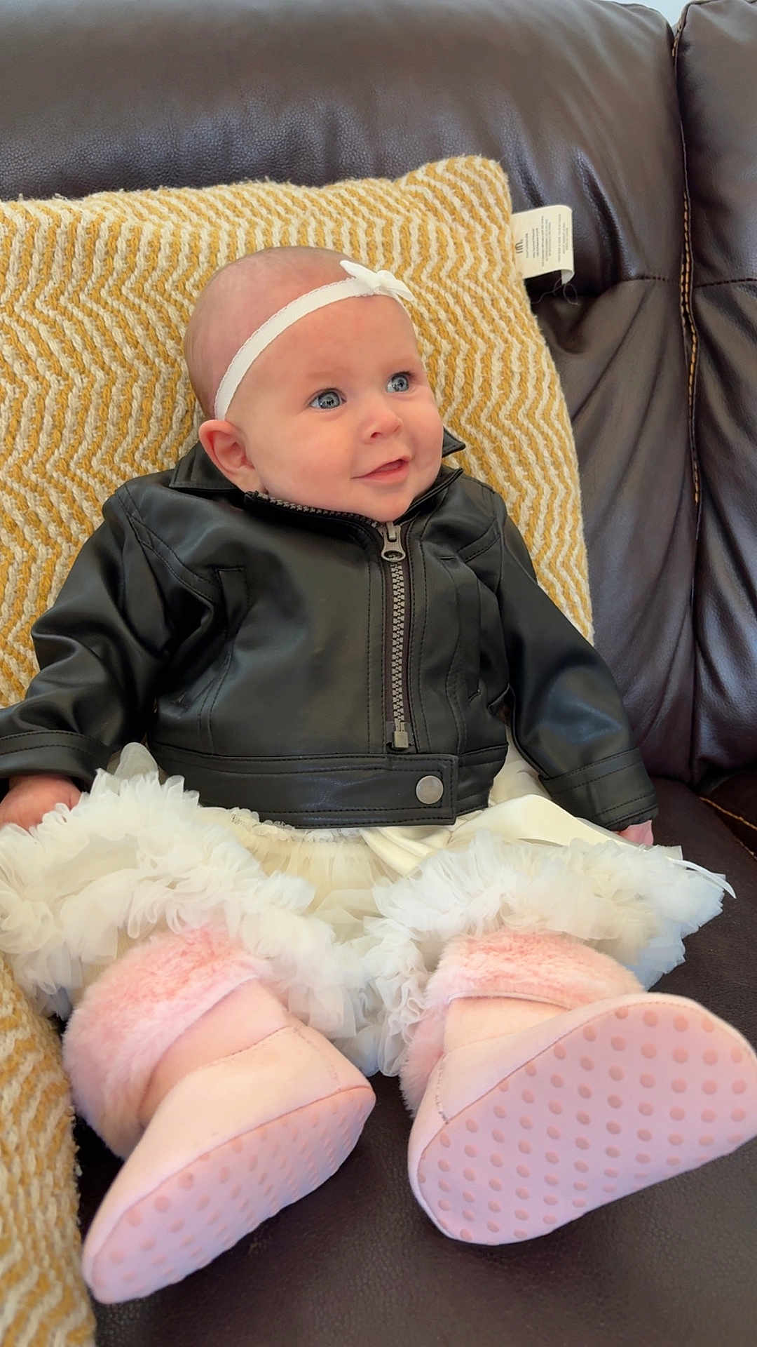 Araya is registered to the contest to win money with this photo: baby, infant, leather_jacket, pink_booties, headband, couch, pillow, smile, blue_eyes, sitting, indoor, clothing, cute, portrait, child, soft_toys, fashion, leather, happy, cozy