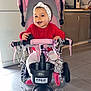 Leecya a rejoint le concours — aidez-le/la à gagner de superbes lots ! baby, child, tricycle, pink, ribbons, headband, red_sweater, indoor, kitchen, floor_tiles, happy, smiling, toy, pedals, seat, handlebars, footrests, person, face, window_light