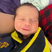 Daelyn joined the competition — help win amazing prizes! baby, newborn, infant, smile, eyes_closed, swaddle, blanket, bed, plaid, purple_bedding, yellow_and_black, closeup, face, hair, cheeks, caretaker_arm, cozy, sleeping, portrait, peaceful