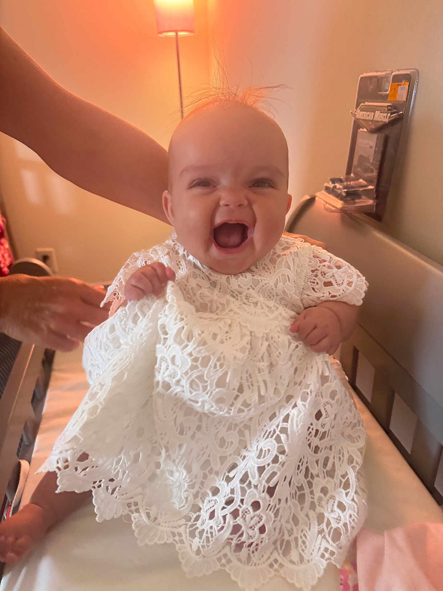 Nova Brielle is registered to the contest to win money with this photo: baby, child, smiling, white_dress, lace, bed, lamp, indoor, person, happy, supporting_hand, infant, cute, portrait, human, clothing, furniture, warm_light, expression, sitting