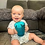 baby, blue_eyes, carpet, child, clothing, couch, cup, cute, furniture, happy, holding, home, indoor, infant, onesie, person, playful, portrait, sitting, smiling