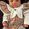 baby, infant, plaid, bow, headband, clothing, cute, portrait, sitting, star_pattern, cushion, indoor, child, young, fashion, cute_outfit, expression, person, face, hands
