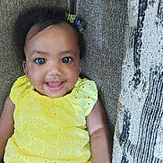 Alani Janae Herrod is registered to the contest to win money with this photo: baby, child, smiling, yellow_dress, couch, indoor, face, happy, person, infant, hair_clip, texture, pattern, seated, cute, portrait, skin, eyebrows, eyes, arm