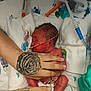 newborn, baby, infant, neonatal_unit, hospital, incubator, medical_tubes, nasal_tube, feeding_tube, oxygen_tubing, monitor_wires, hands, tattooed_hand, tattoo, blanket, swaddle, diaper, tiny_feet, pacifier, adult_hand