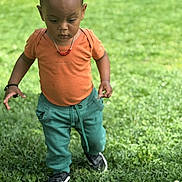Marcus a rejoint le concours — aidez-le/la à gagner de superbes lots ! child, toddler, grass, outdoor, greenery, orange_shirt, green_pants, black_shoes, necklace, bracelet, walking, young, person, portrait, daylight, nature, curious, exploration, casual_clothing, lawn