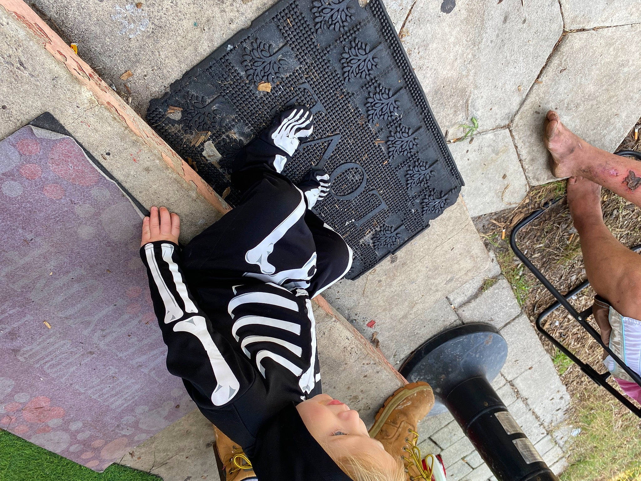 Kol is registered to the contest to win money with this photo: art, asphalt, calf, carmine, finger, flooring, foot, grass, human_leg, knee, leisure, pattern, person, personal_protective_equipment, road_surface, shadow, sidewalk, sitting, thigh, wall