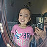 child, girl, smile, mirror, phone, selfie, pink_shirt, butterfly, bedroom, window, curtains, bed, quilt, face, person, reflection, happy, hair, light, casual