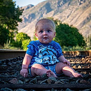Dallas joined the competition — help win amazing prizes! baby, child, infant, portrait, sitting, outdoor, mountains, mountain_view, railway_track, railroad, rocks, nature, landscape, blue_shirt, clothing, shorts, looking_at_camera, wide_eyed, sunlight, trees