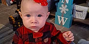 Grace joined the competition — help win amazing prizes! baby, child, indoor, red_bow, plaid_onesie, carpet, toy, stuffed_animal, blue_eyes, holiday_decor, shelf, books, basket, floor, person, cute, infant, winter, home, curious