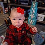 baby, child, indoor, red_bow, plaid_onesie, carpet, toy, stuffed_animal, blue_eyes, holiday_decor, shelf, books, basket, floor, person, cute, infant, winter, home, curious