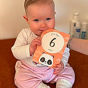 Aria participe au concours pour gagner de l'argent avec cette photo : baby, infant, child, milestone_card, panda_illustration, pink_pants, white_socks, blue_eyes, cute, sitting, hand, bracelet, indoor, soft_lighting, playful, nibbling, milestone, person, smiling, closeup