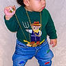 child, toddler, portrait, standing, curly_hair, fashion, sweater, jeans, sneakers, gold_chain, bracelet, ring, sunglasses, toy_cars, indoor, wall, full_body, side_profile, serious_expression, streetwear
