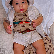 Kayden joined the competition — help win amazing prizes! baby, child, infant, portrait, sitting, lying_down, fashion, designer_clothing, hat, bucket_hat, sunglasses, necklace, gold_chain, sandals, bed, blanket, indoors, smiling, luxury, gucci