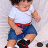 Kayden is registered to the contest to win money with this photo: child, toddler, portrait, curly_hair, sitting, fashion, gold_chain, bracelet, white_shirt, denim_shorts, red_belt, sneakers, sunglasses, accessories, fluffy_blanket, indoor, close_up, looking_down, casual_clothing, fashionable