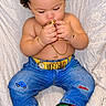 baby, child, infant, curly_hair, sitting, lying_down, portrait, face, eyes_closed, holding_object, snack, gold_jewelry, bracelet, necklace, denim, jeans, sneakers, green_shoes, fashion, blanket