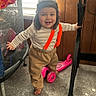 toddler, child, smiling, standing, indoors, portrait, face, hat, winter_clothing, striped_shirt, pants, barefoot, scooter, pink_toy, desk, exercise_bike, window, carpet, home, happy