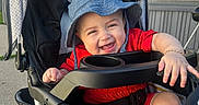 Jeremy Arroyo joined the competition — help win amazing prizes! baby, black_stroller, blue_hat, bracelet, child, cute, hand, happy, hat, infant, joyful, legs, outdoor, person, playful, red_clothing, seatbelt, smiling, stroller, sunlight