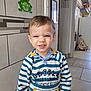 child, toddler, smiling, indoor, striped_clothing, hoodie, face, person, tile_wall, toy, floor, decor, hair, cute, expression, laugh, young_child, casual, standing, playful