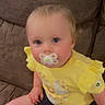 baby, blond_hair, blue_eyes, casual_clothing, child, comfortable, couch, curious, cute, denim_shorts, furniture, holding_object, indoor, infant, pacifier, portrait, rosy_cheeks, sitting, small_object, yellow_shirt