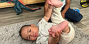 Kash is registered to the contest to win money with this photo: baby, child, floor, rug, toy, dinosaur, hand, foot, clothing, toddler, person, indoor, wooden_floor, cabinet, sitting, playful, curious, casual, home, carpet