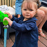 Salomé participe au concours pour gagner de l'argent avec cette photo : toddler, child, woman, scooter, blue_dress, denim_jacket, glasses, balloons, outdoor, deck, wooden_floor, toy, person, footwear, fence, green, blue, hair, face, expression
