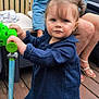 toddler, child, woman, scooter, blue_dress, denim_jacket, glasses, balloons, outdoor, deck, wooden_floor, toy, person, footwear, fence, green, blue, hair, face, expression