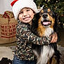 child, dog, smiling, santa_hat, christmas_tree, holiday, festive, camouflage_clothing, hug, indoor, decorations, lights, joy, friendship, fur, kneeling, happy, canine, celebration, portrait