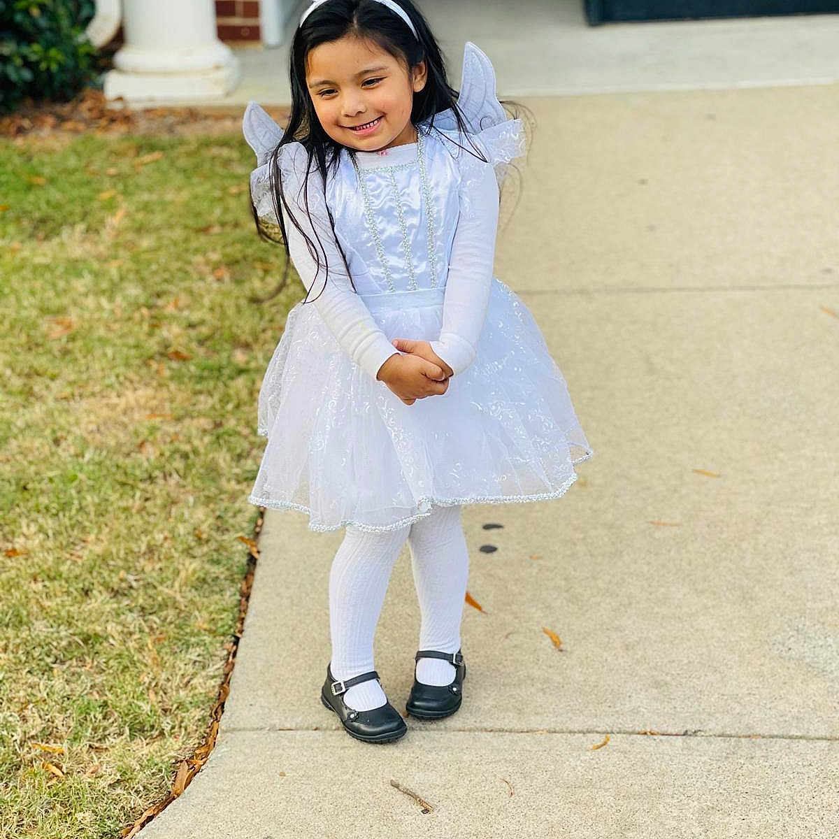Victoria Huerta is registered to the contest to win money with this photo: angel_costume, black_shoes, child, costume, cute, daylight, fashion, girl, grass, halo, happy, holiday, long_hair, outdoor, portrait, pose, sidewalk, smiling, tights, white_dress