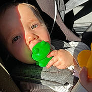 Eléa a rejoint le concours — aidez-le/la à gagner de superbes lots ! baby, infant, child, car_seat, green_toy, frog_toy, pacifier_like_toy, hand, seatbelt, sunlight, shadow, closeup, portrait, cheek, nose, clothing, plastic_toy, car_interior, buckle, cute