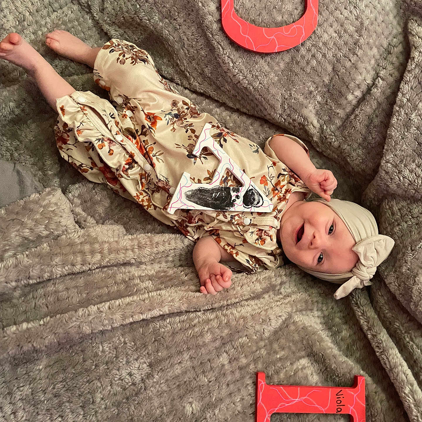 Viola is registered to the contest to win money with this photo: baby, blanket, child, cozy, cute, floor, floral_outfit, foot, hand, handmade_letters, happy, headband, indoors, infant, lying_down, portrait, red_letters, skin, smiling, soft_texture