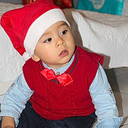 Marius participe au concours pour gagner de l'argent avec cette photo : child, toddler, santa_hat, red_bow_tie, red_sweater, blue_shirt, toy, floor, tile_floor, gift_box, holiday, christmas, indoor, person, cute, festive, sitting, young_child, playing, holiday_decoration