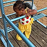 Naomi is registered to the contest to win money with this photo: toddler, child, playground, outdoor, yellow_clothing, curly_hair, blue_metal, wooden_platform, exploring, daylight, summer, young_child, play_equipment, casual_clothing, nature, grass, metal_bars, focused, cute, active