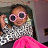 Naomi joined the competition — help win amazing prizes! toddler, child, sunglasses, pink, flower, leopard_print, towel, indoor, person, curly_hair, smile, hand, holding, string_lights, room, window, wall, doorway, decor, casual_clothing