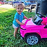 Annabelle joined the competition — help win amazing prizes! toddler, child, baby, smiling, outdoor, grass, toy_vehicle, toy_truck, pink_truck, dog, pet, driveway, residential_area, blue_truck, vehicles, summer, sunlight, portrait, playtime, outdoors